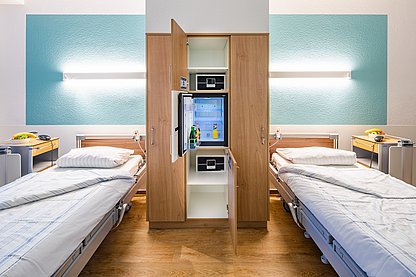 Ein Zwei-Bett-Zimmer der Komfortstation, getrennt durch den zimmereigenen, mit Getränken und Snacks gefüllten Einbau-Kühlschrank