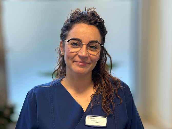 Porträt einer jungen Frau mit Brille und braunen Locken in dunkelblauem Pflege-Kasack