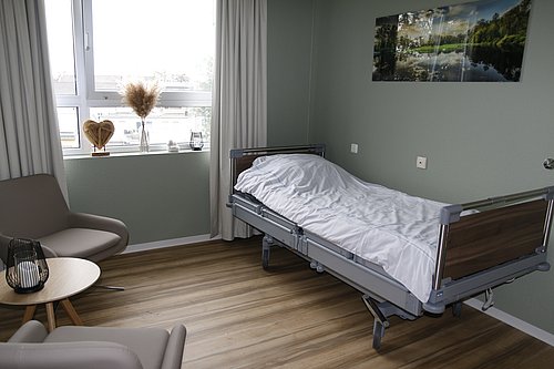 Ein hell eingerichtetes, in Erdtönen gehaltenes Zimmer mit einem Bett, einem Sessel und Fenster.