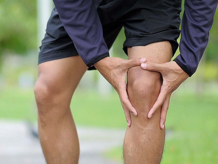 Ein Mann in Laufkleidung hält sich das linke Knie wegen Knieschmerzen