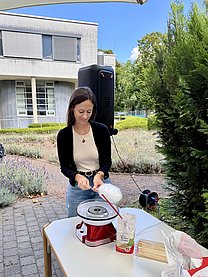 Eine junge Frau steht in einem Krankenhausgarten an einer Zuckerwattenmaschine.