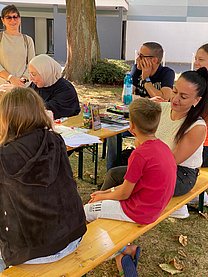 Mehrere Menschen auf sitzen an einer Bierzeltgarnitur, im Vordergrund schminkt eine Frau einem Jungen das Gesicht.