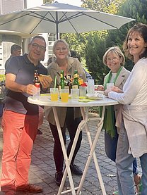 Drei Frauen und ein älterer Mann (links) stehen an einem Stehtisch.