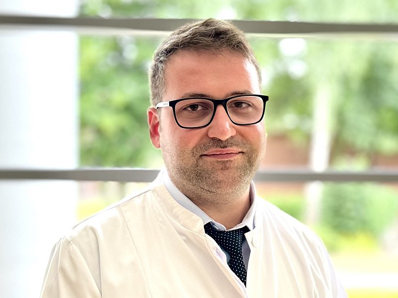 Porträt eines jungen Arztes in Arztkittel, darunter trägt er ein hellblaues Hemd und eine Krawatte