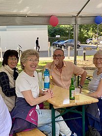 Drei ältere Damen und ein mittelalter Herr sitzen an einer Bierzeltgarnitur.