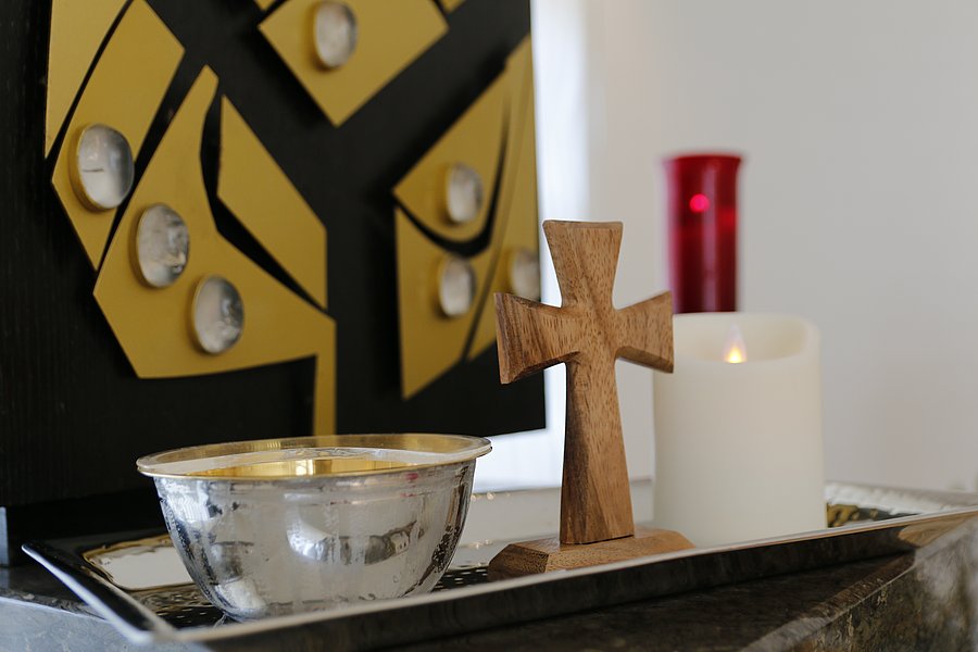 Nahaufnahme von einer Kommunionsschale, einem Holzkreuz und einer LED-Kerze