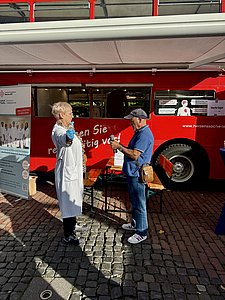 Eine Diabetesberaterin im weißen Kittel zeigt einem Patienten, wie er kleine Hanteln für kurze Bewegungseinheiten benutzt.