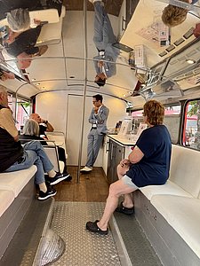 Ein Arzt im Inneren eines Doppeldeckerbusses hält vor einigen Zuhörern einen Vortrag.