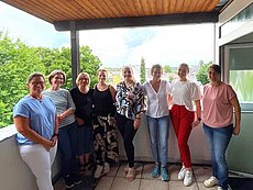 Acht Frauen (Wundmanagerinnen) jeden Alters in Zivilkleidung auf einem Balkon eines Krankenhauses