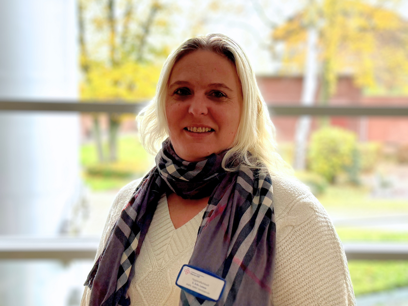 Porträtfoto einer Frau mittleren Alters mit blondierten langen Haaren, einem weißen Strickpulli und einem graukarierten Schal