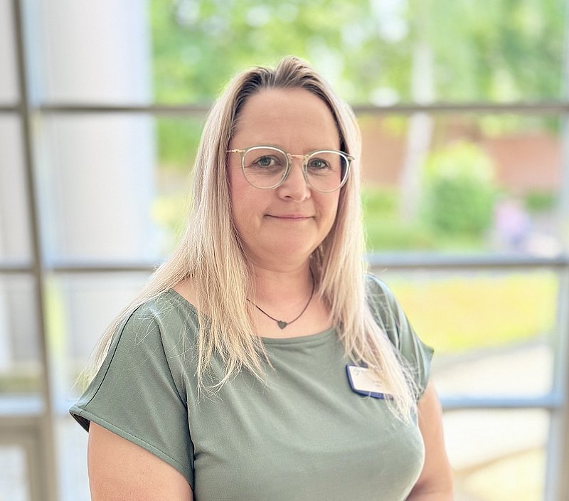 Porträt einer Frau mit blonden Haaren und Brille mit mintfarbenden Oberteil