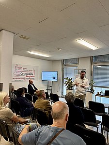 Ein Mann in weißem Hemd steht vor einem Publikum und hält einen medizinischen Vortrag.