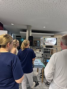Medizinisches Personal in Arbeitskleidung betrachtet gemeinsam einen Monitor, der ein endoskopische Aufnahme eines (künstlichen) Meniskus zeigt zeigt.