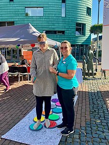 Eine Frau hält eine andere Frau, die eine Augenbinde trägt und über verschieden Sensorikplatten steigt. 